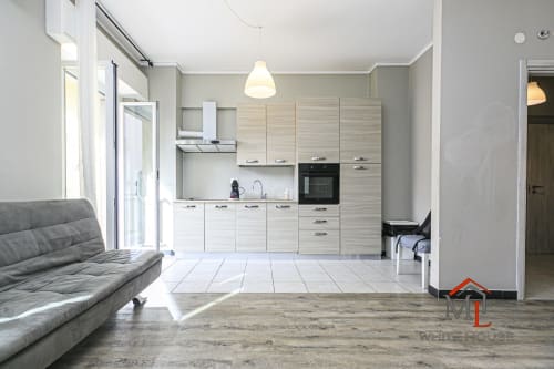 Moderno monolocale a Genova con cucina a vista, divano grigio, pavimenti in legno e eleganti luci a sospensione