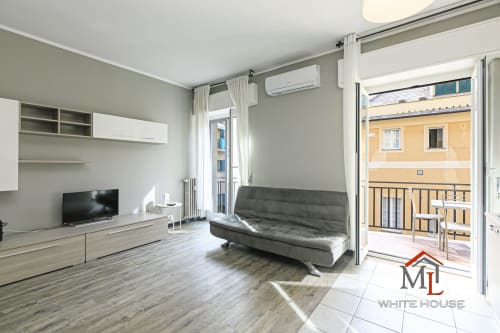 Soggiorno moderno nella Ulivo House, appartamento a Genova con divano grigio, TV, angolo cottura e balcone con vista sulla città