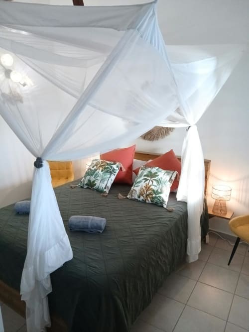 Lit à baldaquin aux voilages blancs aériens, coussins aux motifs tropicaux et accents rouges à la Villa Ti Soley Mafanga, Bouillante
