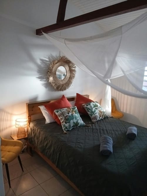Chambre avec lit à baldaquin, miroir décoratif et coussins rouges à la Villa Ti Soley Mafanga, Bouillante