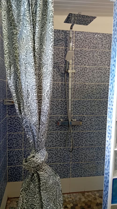 Salle de bain moderne avec douche à mosaïques, pomme de douche pluie et rideau à motifs décoratifs à LÉZILÉ