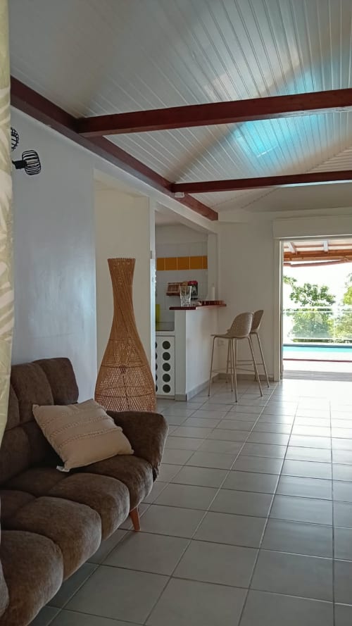 Intérieur de villa moderne avec fauteuil marron, lampe tressée, bar et vue sur mer par portes vitrées à LÉZILÉ, Bouillante