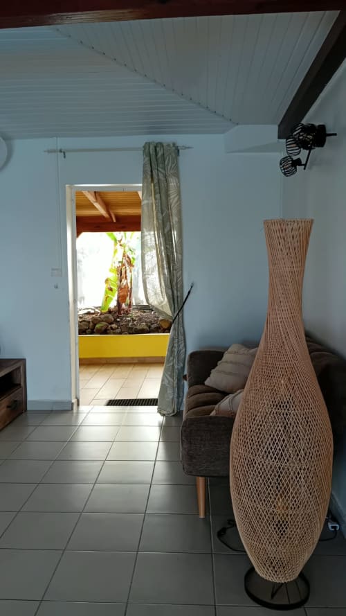 Intérieur de villa moderne en Guadeloupe avec vase tressé, rideaux gris, mobilier foncé et vue mer par la porte
