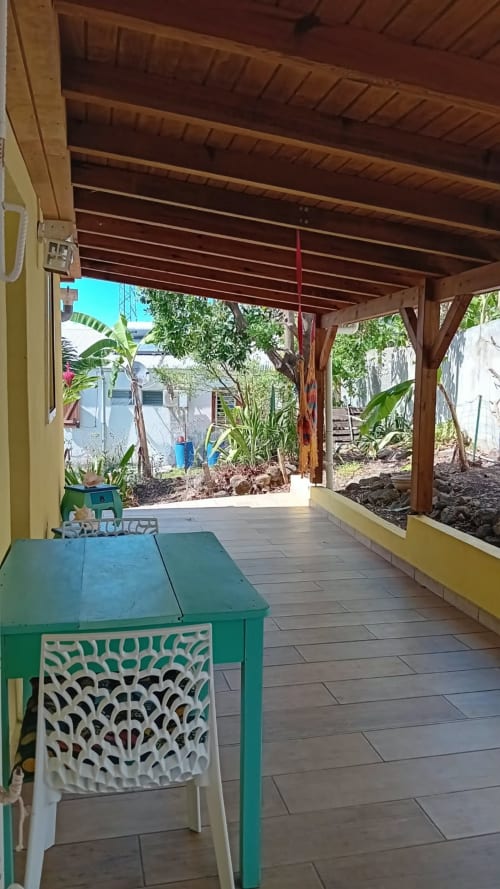 Terrasse couverte en bois avec chaise et table vertes à la Villa Ti Soley Mafanga, Bouillante, vue sur jardin tropical et mer