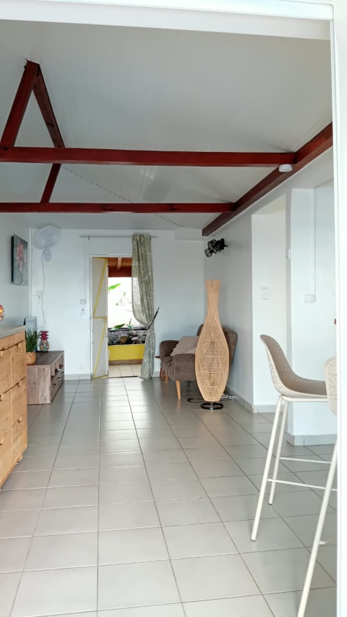 Intérieur de villa moderne avec poutre rouge au plafond, sol carrelé, mobilier en bois et décoration tissée à LÉZILÉ à Bouillante,