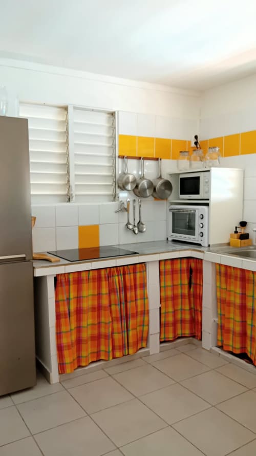 Cuisine lumineuse aux accents jaunes et orangés, armoires blanches, appareils en acier inoxydable et rideaux à motifs à la Villa