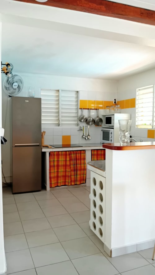 Cuisine lumineuse de la Villa Ti Soley Mafanga avec armoires blanches, accents orange, appareils inox et carrelage