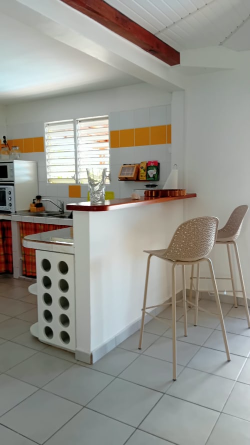 Cuisine moderne avec accents orange, îlot central, bar et électroménagers blancs à Villa Ti Soley Mafanga, Bouillante