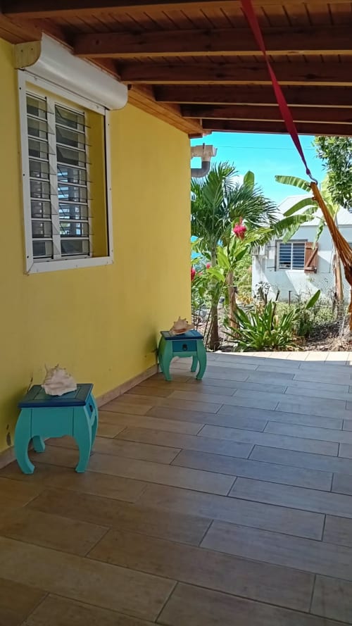 Terrasse de villa jaune avec tables turquoise, plantes tropicales et vue sur la mer à Bouillante, Guadeloupe