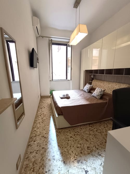 Camera da letto moderna nell'appartamento Matilde Sweet Home a Roma, con letto marrone, armadi bianchi, lampada a sospensione e pavimento in terrazzo