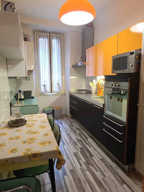 Cucina moderna con mobili arancioni, elettrodomestici neri, tovaglia con girasoli e zona pranzo in Matilde Sweet Home
