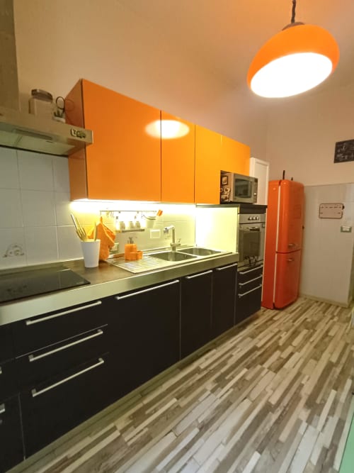 Cucina moderna dell'appartamento Sweet Home Rome con mobili arancioni, unità inferiori nere, frigorifero rosso e illuminazione a sospensione