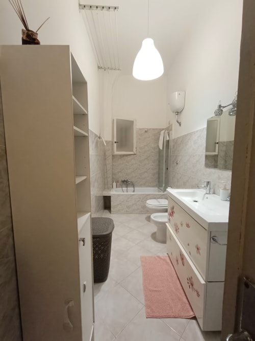 Bagno moderno nell'appartamento Matilde Sweet Home a Roma, con vanità bianca, piastrelle in marmo, toilette, vasca e lampade a sospensione