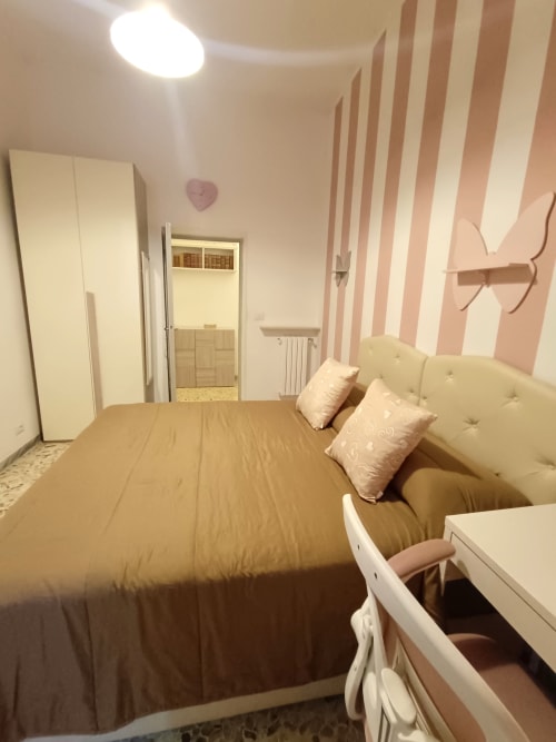 Camera da letto Matilde Sweet Home a Roma con letto rivestito in crema, pareti a righe rosa, armadio e bagno en-suite