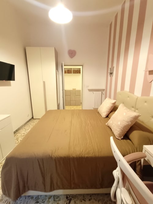 Camera da letto Matilde Sweet Home a Roma con letto queen, testata bianca, pareti a righe rosa, guardaroba e TV