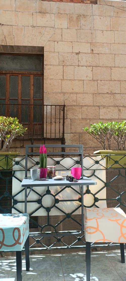Alicante balcony with decorative furniture, pink accents, potted plants, and stone building facade
