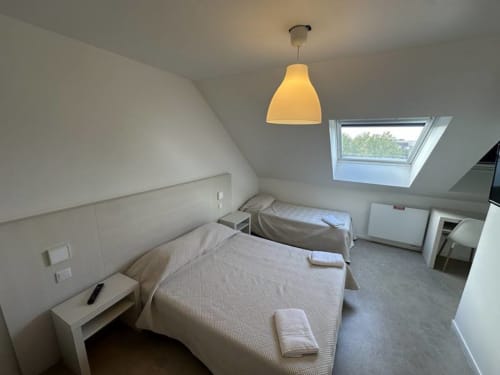 Chambre triple Hotel Motelia à Moissy-Cramayel avec deux lits, puits de lumière, suspension et décor épuré minimaliste
