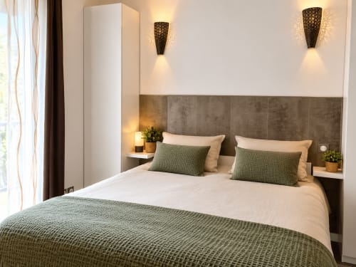 Chambre moderne à la Maison D'hôtes Coeur D'hérault avec lit queen, tête de lit grise, accents verts et appliques murales design.