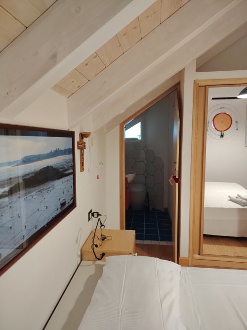 Camera da letto in mansarda luminosa con soffitto spiovente, TV che mostra paesaggio innevato, porte in legno verso bagno e corridoio, letto