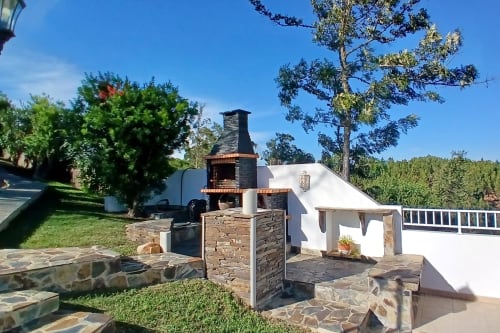 Lareira de pedra tradicional, edifício branco e jardins na quinta-hotel SELÃO DA EIRA em São Teotónio, Portugal