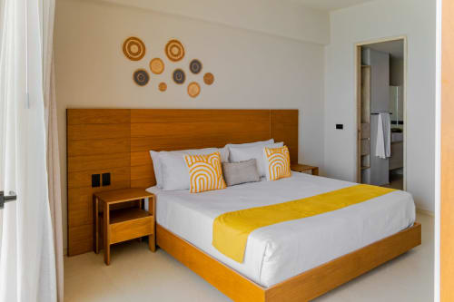 Dormitorio moderno en Condominio Marlica, Manzanillo, con cama de marco de madera, detalles amarillos y platos tejidos decorativos sobre blanco