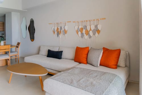 Sala moderna del Condominio Marlica con sofá seccional crema, cojines naranjas, mesa de madera y arte de macramé en la pared