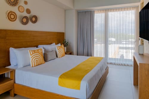Moderno dormitorio en Condominio Marlica, Manzanillo, con cabecero de madera, detalles en amarillo y balcón con vista al océano