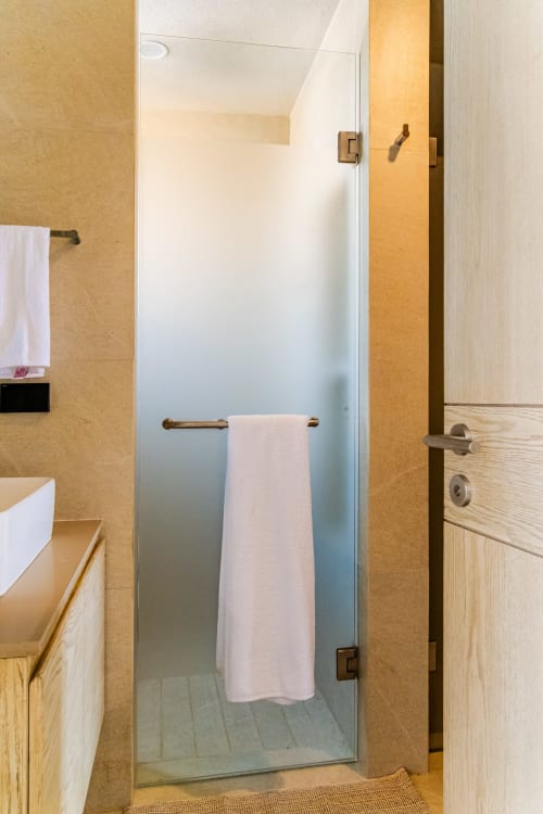 Moderno baño con ducha abierta, puerta de vidrio esmerilado y accesorios en bronce en Condominio Marlica, Manzanillo