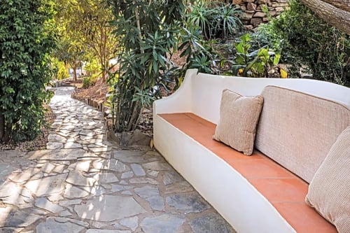 Área de estar externa aconchegante em Casa Cisne com sofá estofado bege no pátio de terracota, vistas do jardim exuberante e caminho de pedra