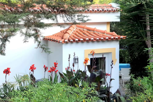 Vista do jardim Casa Cisne com lírios vermelhos, casarão de paredes brancas, telhas de terracota, Alentejo rural em Portugal