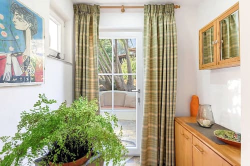 Quarto luminoso na Casa Cisne com cortinas xadrez verdes, planta em vaso, móveis de madeira e vista do jardim pelas portas de vidro