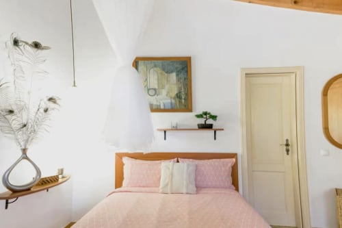 Quarto aconchegante na Casa Cisne com roupa de cama rosa, cabeceira de madeira, paredes brancas, quadros emoldurados e decoração rústica em SELÃO DA