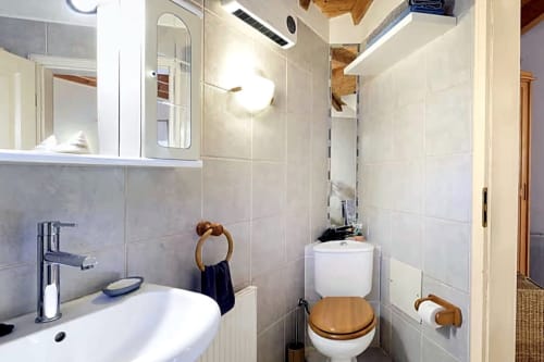 Banheiro moderno com pia branca, vaso sanitário com assento de madeira e chuveiro na Casa Cisne do hotel rural SELÃO DA EIRA, Portugal