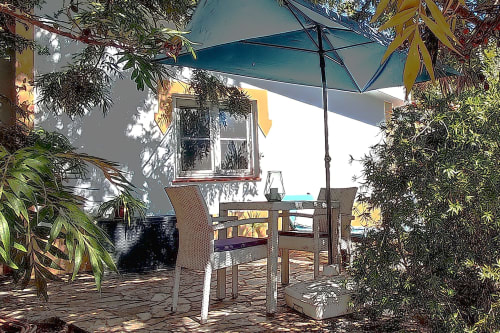 Área de repouso sombreada do hotel rural SELÃO DA EIRA no Alentejo, Portugal, com guarda-sol, mesa e vegetação exuberante