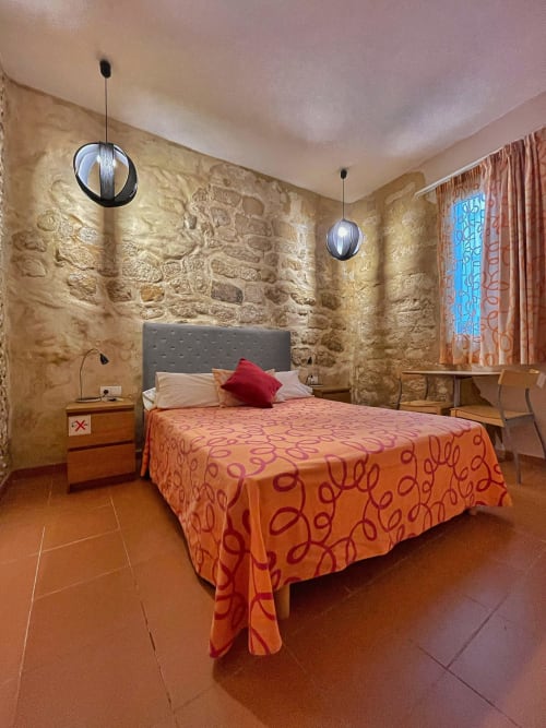 Chambre double à la Pensión Alicante San Nicolás avec murs en pierre, literie orange, luminaires suspendus et mobilier en bois