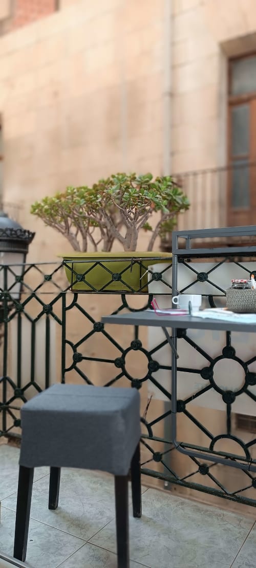 Area salotto sul balcone della Pensión Alicante San Nicolás con albero in vaso, ringhiere geometriche nere e facciata beige