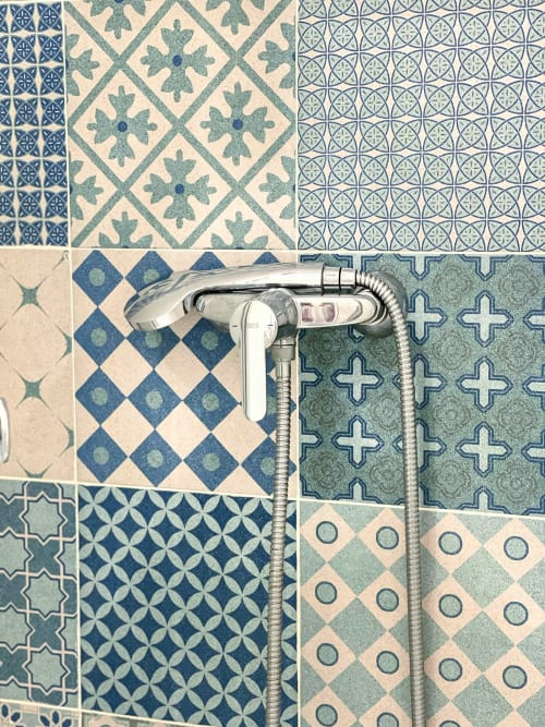 Soffione della doccia cromato montato sulle piastrelle decorative blu e bianche del bagno della Pensión Alicante San Nicolás
