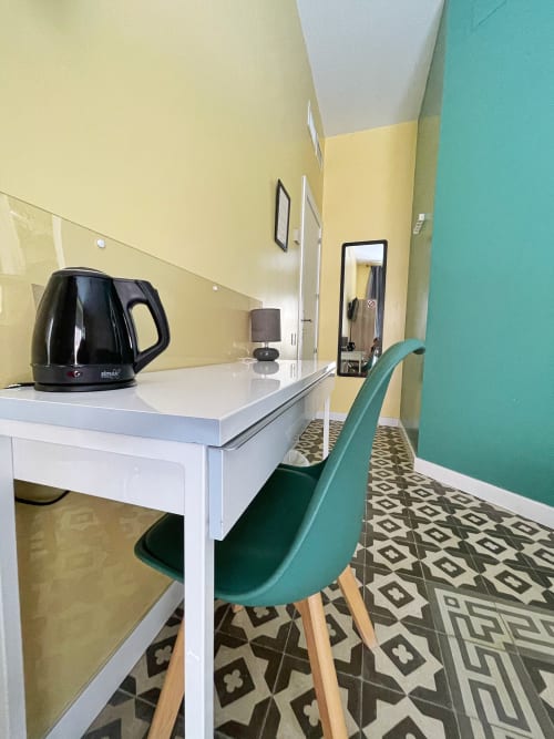 Scrivania moderna di hotel con bollitore nero, lampada e sedia turchese presso Pensión Alicante San Nicolás