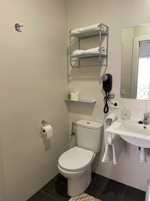 Bagno moderno della Pensión Alicante San Nicolás con wc bianco, lavandino, specchio, porta asciugamani con biancheria e elementi neri