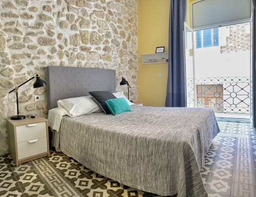 Camera moderna nella Pensión Alicante San Nicolás con muri in pietra, letto grigio, accesso al balcone e vista sulla città