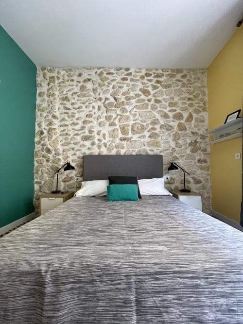 Camera moderna presso la Pensión Alicante San Nicolás con parete in pietra, letto grigio, cuscino azzurro e pareti colorate