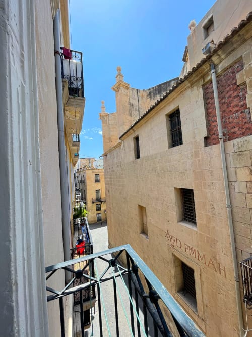 Vista dal balcone di una strada stretta nel centro storico di Alicante con edifici storici in pietra e cielo azzurro della Pensión Alicante