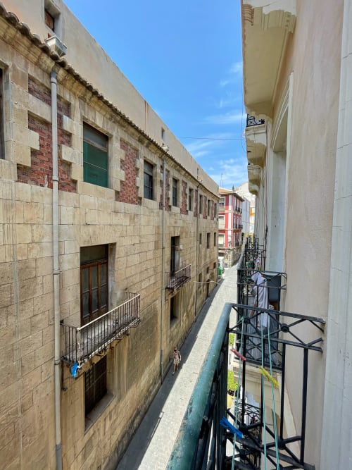 Vista dal balcone di una stretta via di Alicante con edifici storici in pietra e facciate colorate, Pensión Alicante San Nicolás