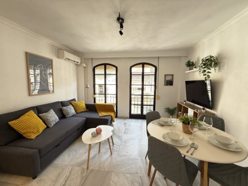 Acogedor apartamento moderno en Fuengirola con sofá negro, mesa de comedor, puertas al balcón y mobiliario contemporáneo