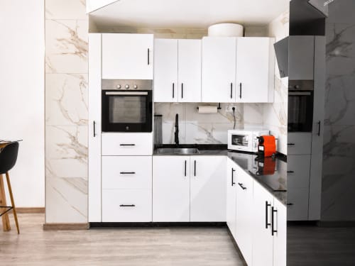 Cocina moderna blanca con paredes de mármol, encimeras negras, electrodomésticos y almacenamiento en Apartamento Lateral Perla