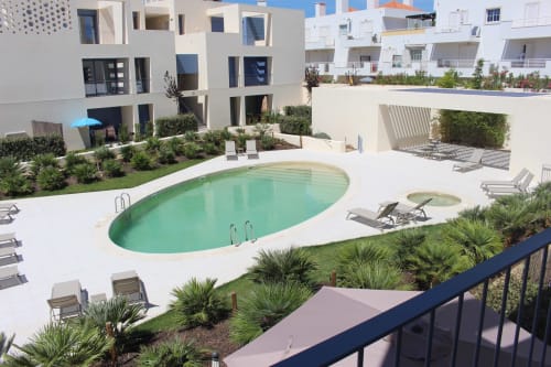 Break Lovers BnB pool area in Tavira with loungers, palm landscaping, and modern white apartments overlooking turquoise water