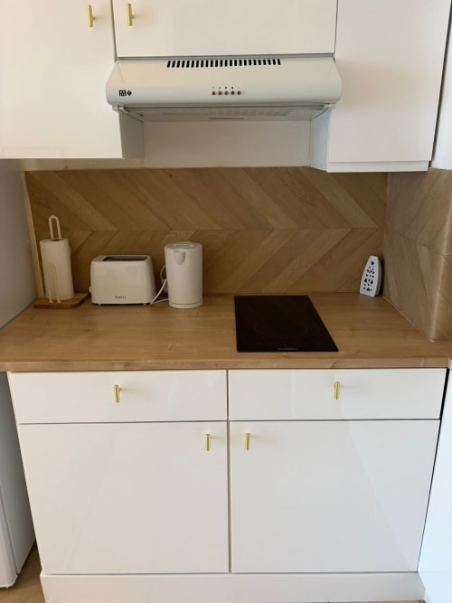 Cuisine moderne avec placards blancs, crédence en bois et appareils électroménagers à l'appartement Le Paradis Des Logis, Pierrefitte