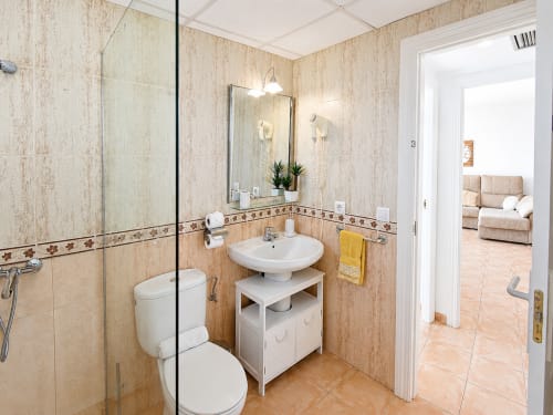 Modern bathroom with beige tile walls, pedestal sink, toilet, and glass shower enclosure at Apartamentos El Calón Playa,