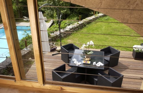 Terrasse extérieure avec mobilier en rotin noir, maison en pierre, pelouse verte et vue sur la piscine aux Chambres d'hôtes Les Pratges, Figeac
