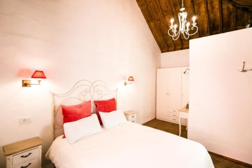 Elegante dormitorio en Casa 1820 con acentos rojos, cabecero ornamentado, lámpara de araña y techo de madera en Santa Cruz